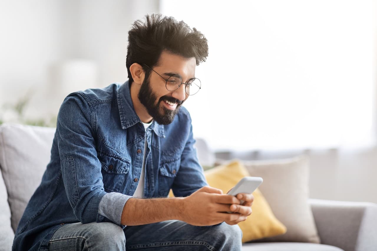 Homem sentado no sofá, mexendo no celular.