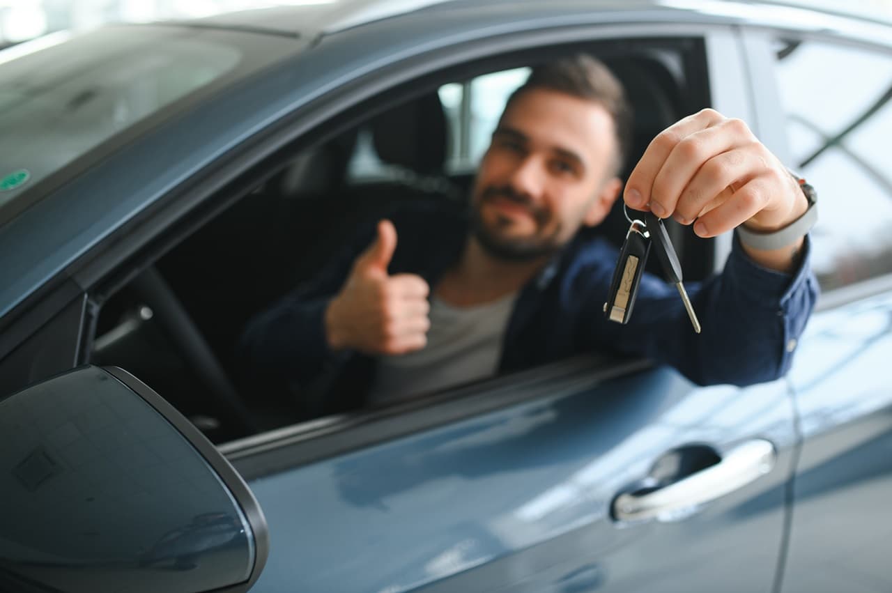 Homem sorrindo dentro do carro, segurando a chave do carro nas mãos