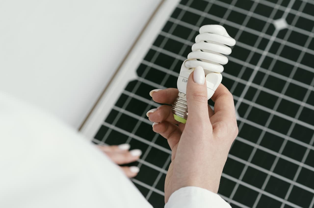 Close-up na mão de uma pessoa segurando uma lâmpada fluorescente econômica em frente a um painel solar.