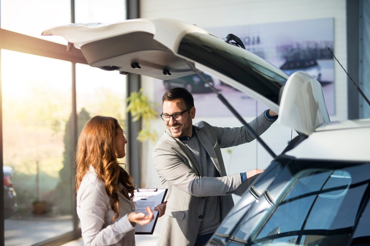 Cliente e vendedor trocando informações ao lado de um carro SUV branco, em uma loja de automóveis.