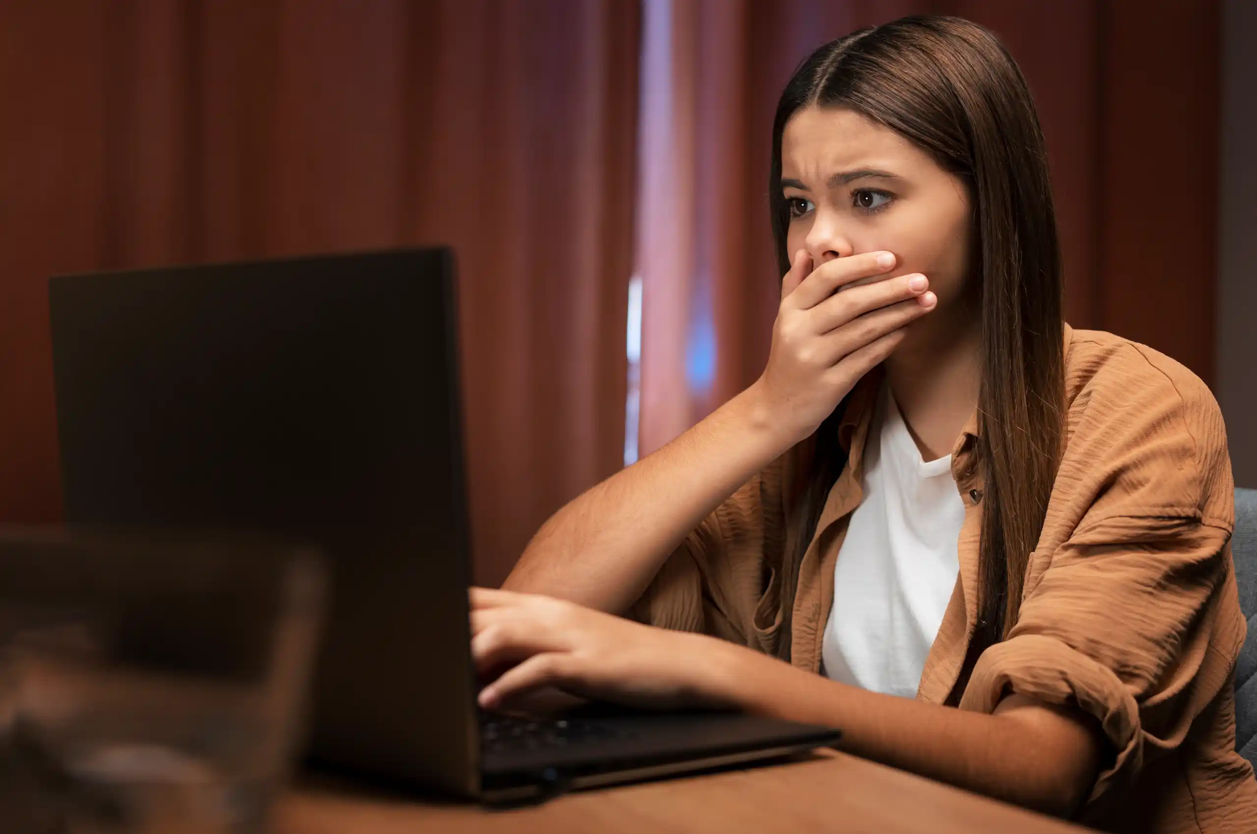 Uma mulher com uma expressão espantada enquanto encara a tela de um notebook.