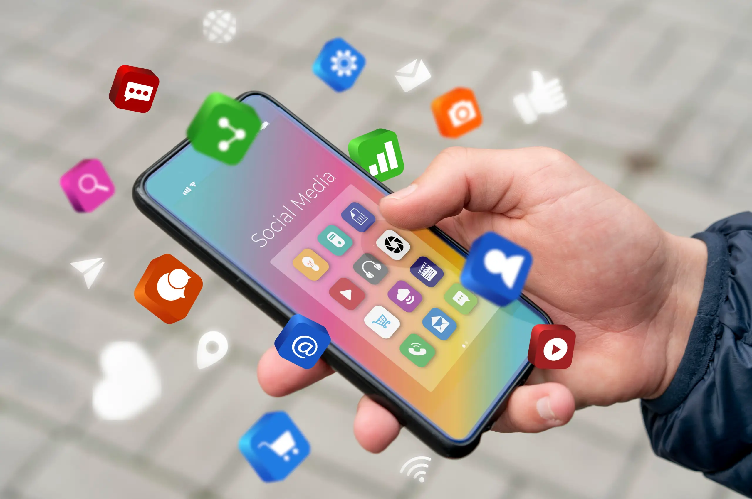 Mão segurando um smartphone com tela clara, cercado por ícones de aplicativos sociais flutuando ao redor, simulação de uso de mídia social.