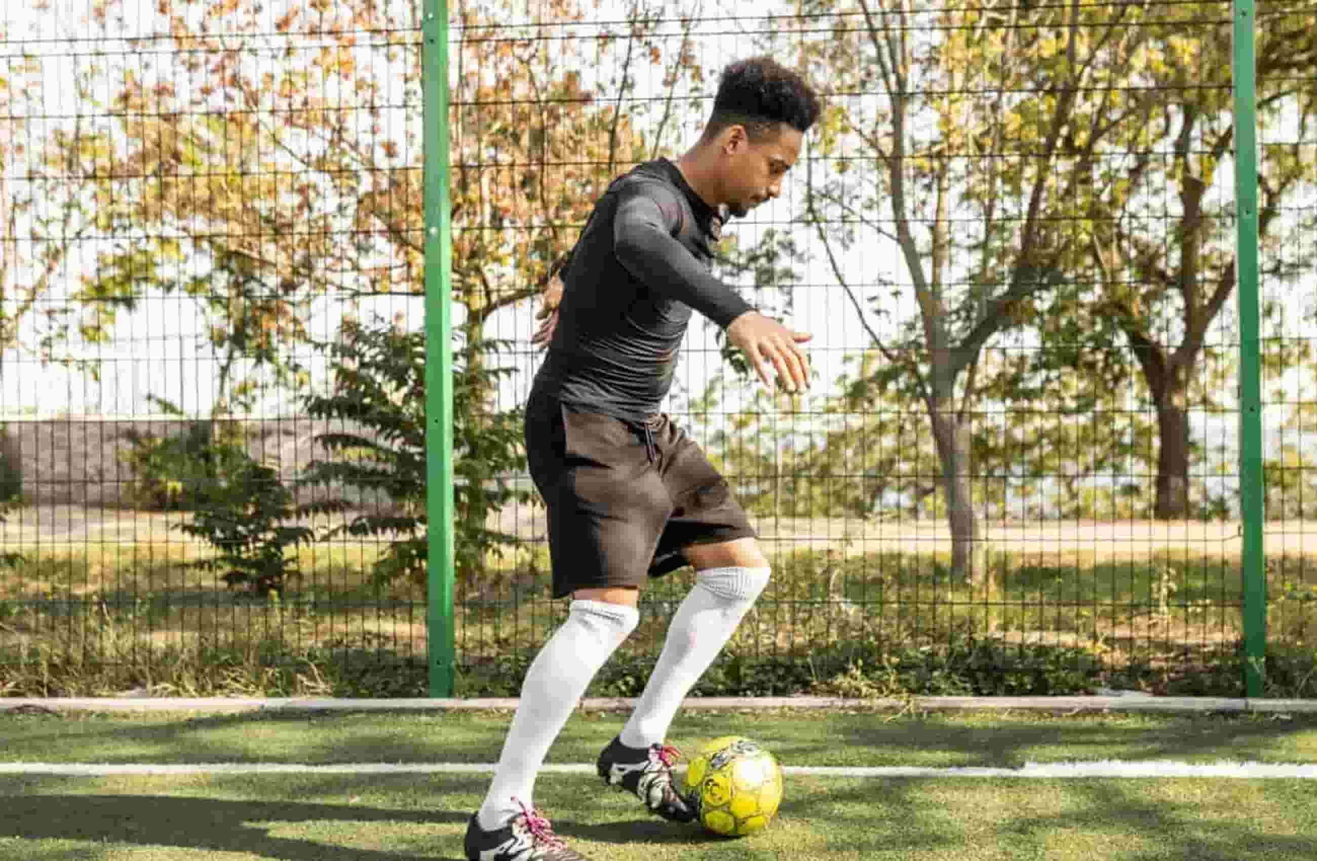 Homem vestido com roupas esportivas está jogando futebol em um campo.