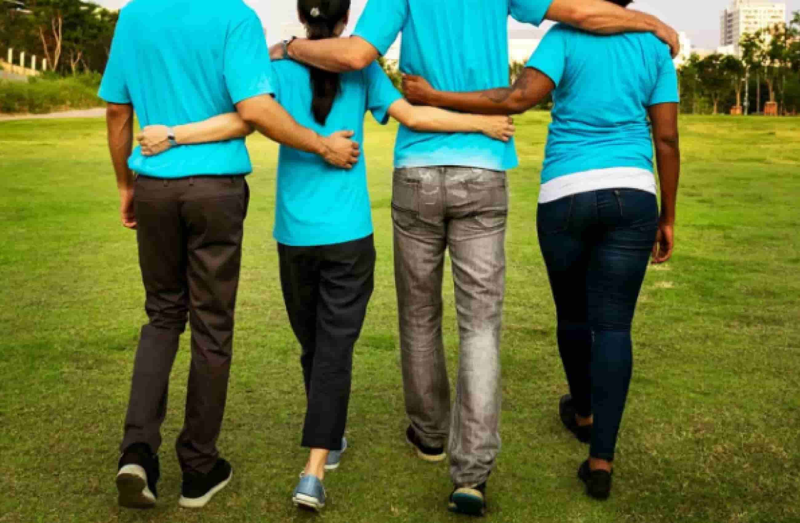 4 pessoas de calça escura e camisa azul de costas andando na mesma direção, um com os braços nas costas dos outros.