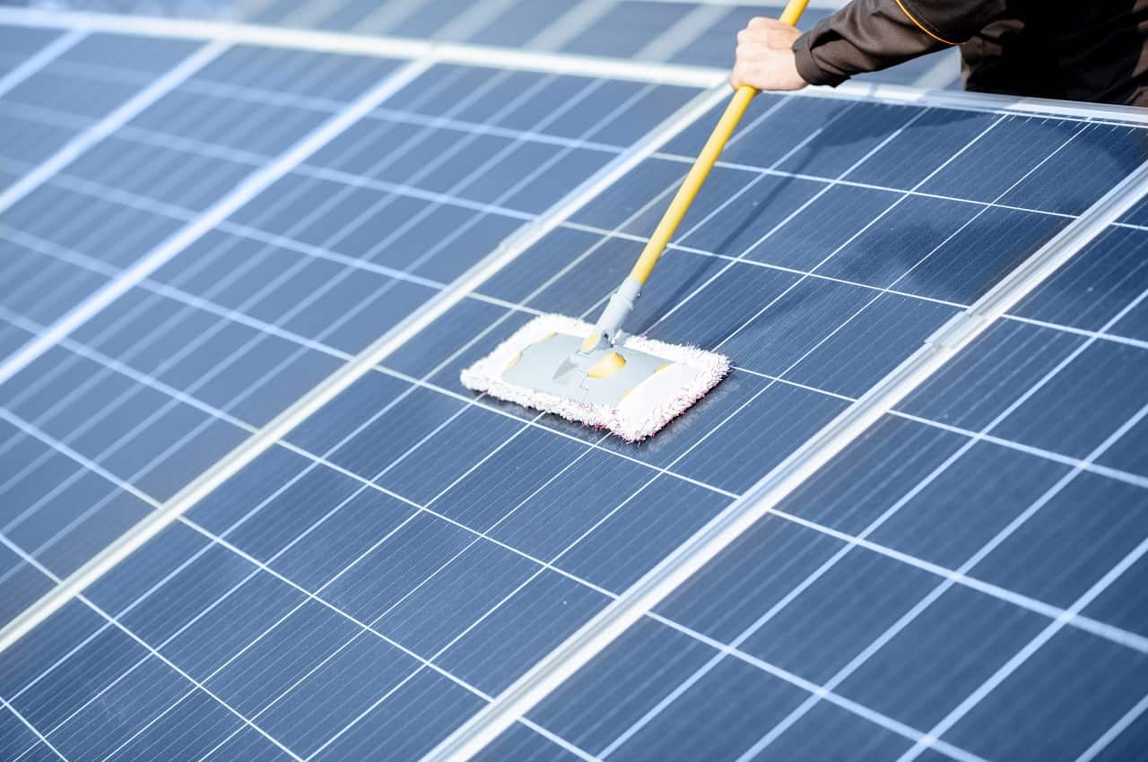 Pessoa (seu rosto não aparece) usando um esfregão amarelo e macio para fazer a limpeza de painéis solares.