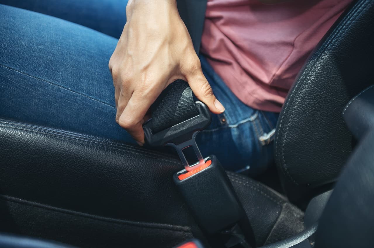 Close de uma mão afivelando o cinto de segurança em um banco de couro preto de um carro.