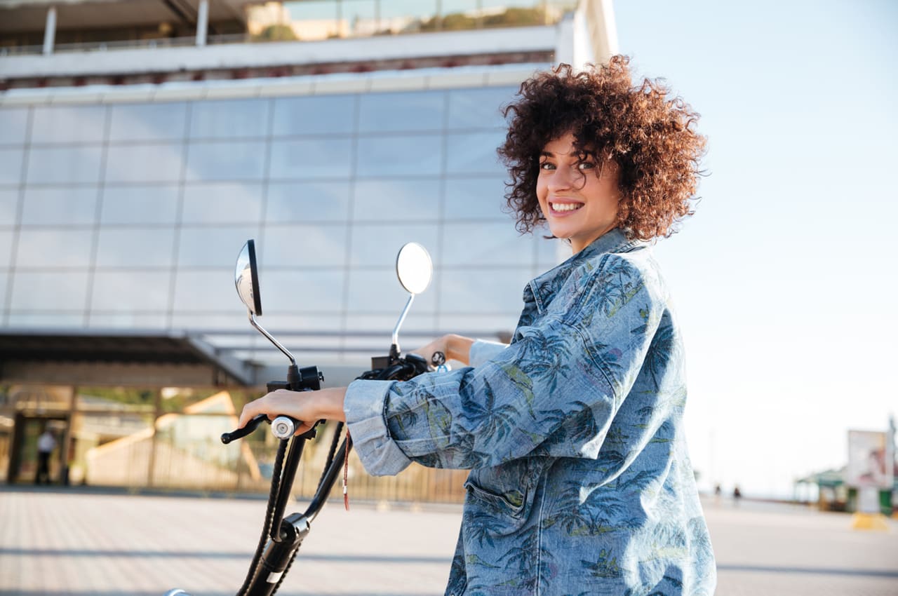 Mulher sorridente em um uma scooter, promovendo a mobilidade e sustentabilidade em uma área urbana.