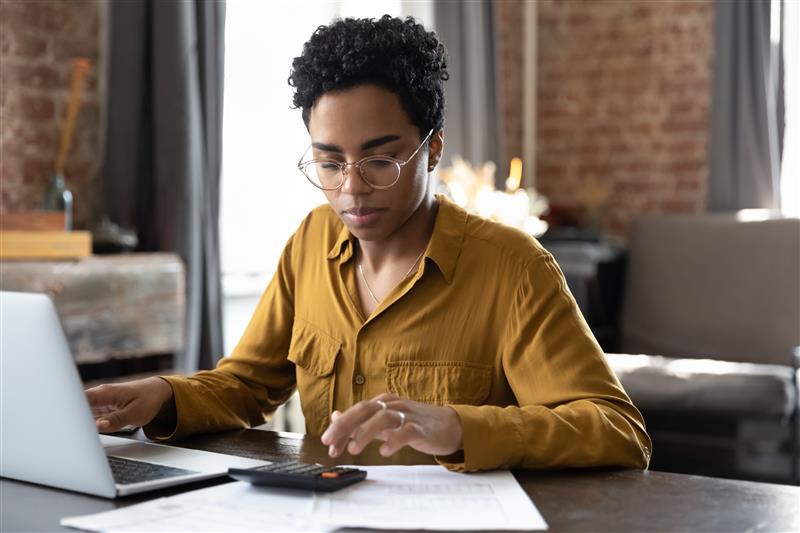 mulher fazendo cálculos com calculadora e notebook em uma mesa