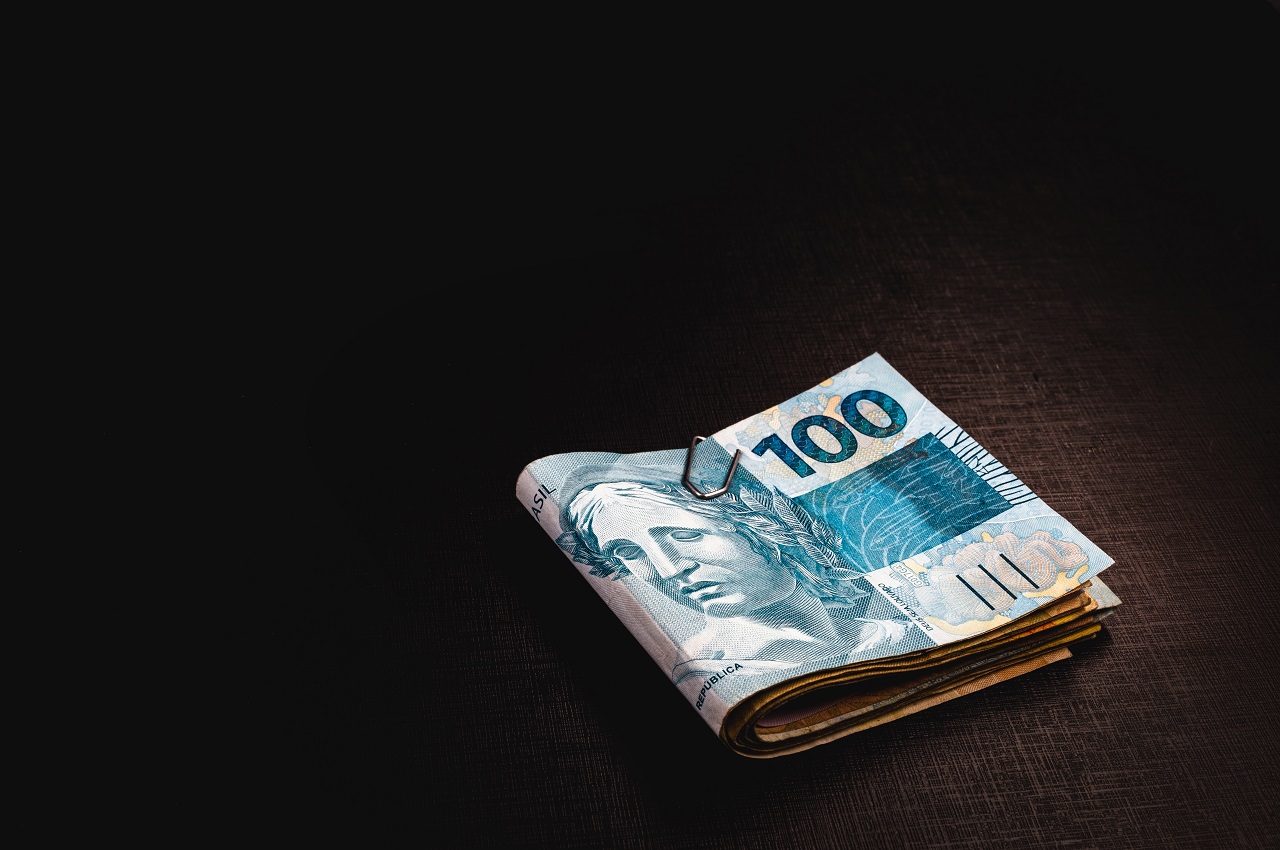Bolo de notas de cem reais (R$100,00) preso com um clipe e em cima de uma mesa de madeira.