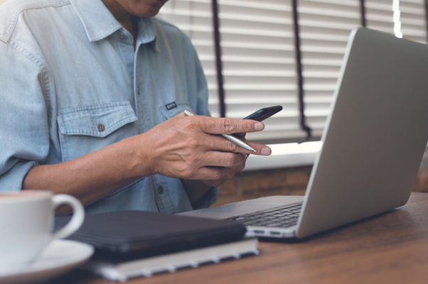 Homem mexendo no celular e com uma caneta apoiada na mão, em ambiente de escritório, vendo se Open Finance é seguro.