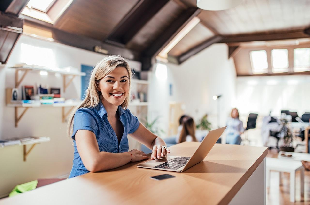A imagem mostra uma mulher sorridente usando seu laptop.