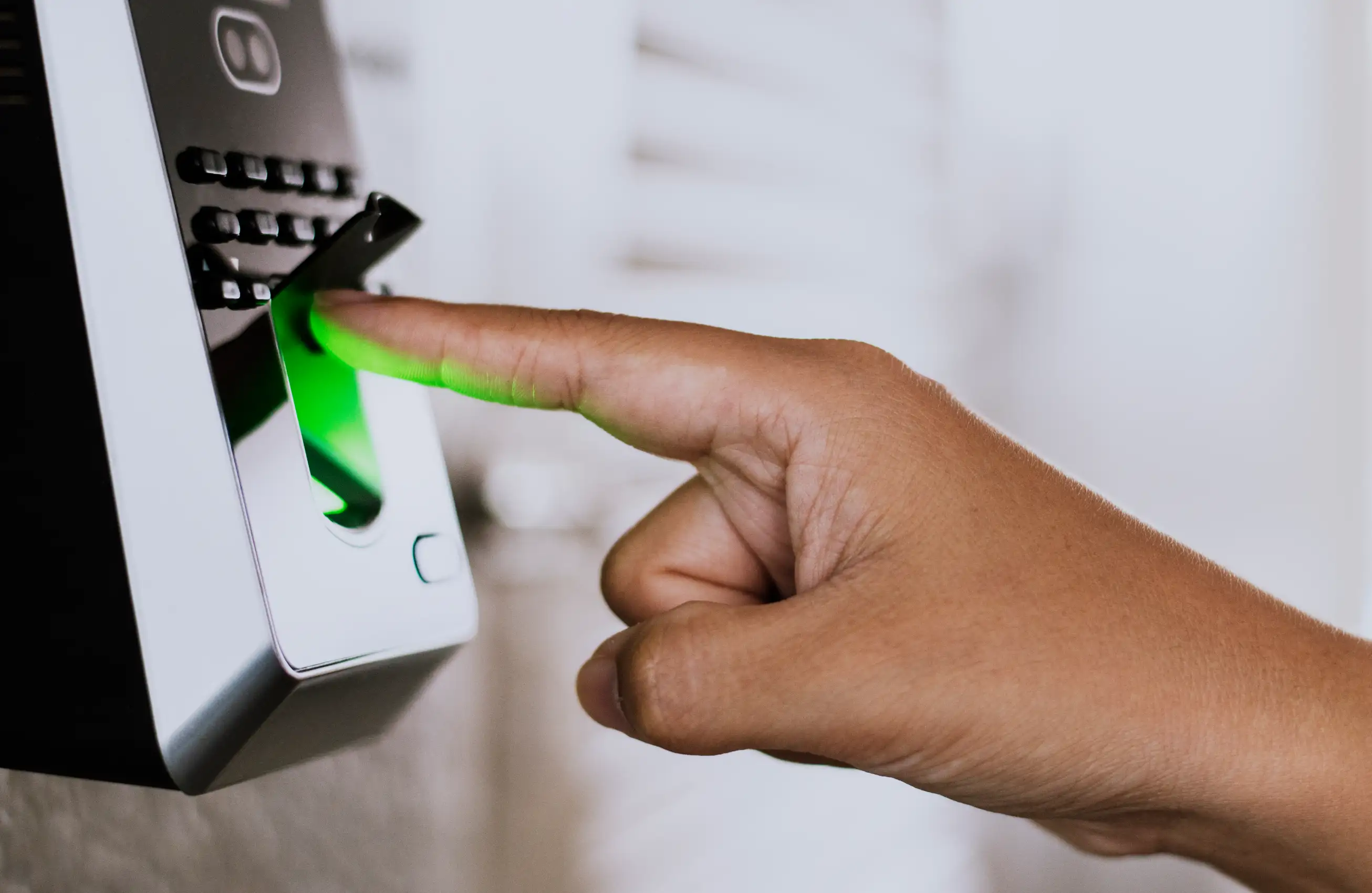 Mão pressionando um leitor biométrico de impressão digital iluminado em verde, com o dedo inserido no sensor.