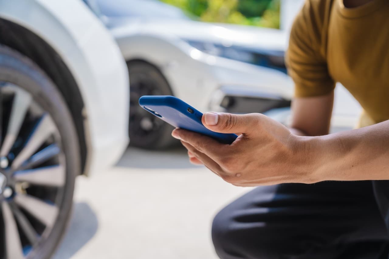 homem segurando um celular, com carro ao fundo