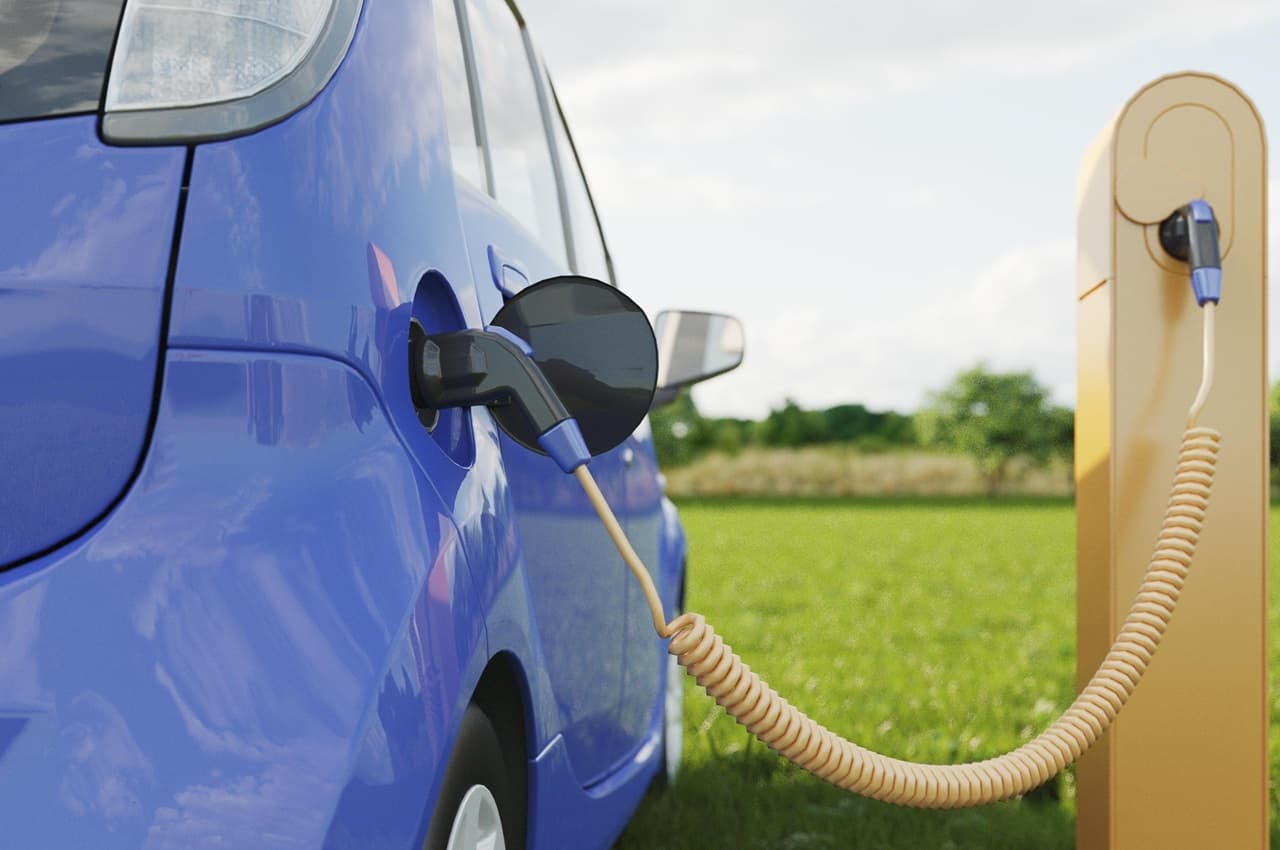Carro elétrico azul conectado a uma estação de carregamento amarela, em um campo verde.