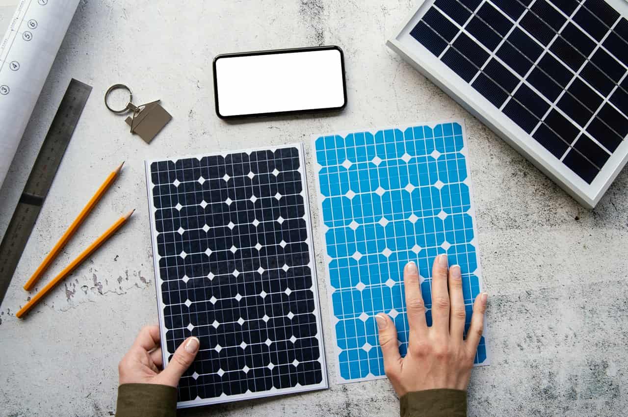 Vista superior de mãos segurando impressões de painéis solares em uma mesa com smartphone, lápis e um pequeno painel solar real.