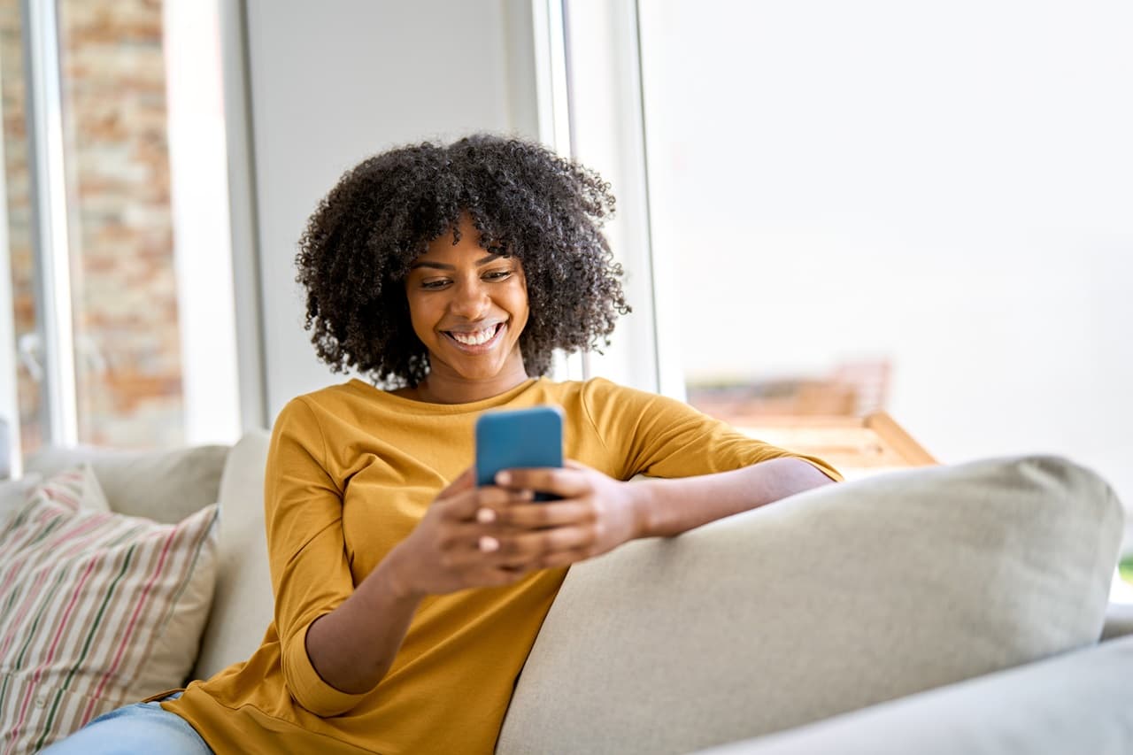 Pessoa usando celular sentada no sofá, representando consulta ou acompanhamento de finanças pessoais
