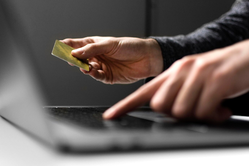Uma imagem close-up em um notebook sobre uma mesa. Um homem está digitando enquanto segura um cartão de crédito.