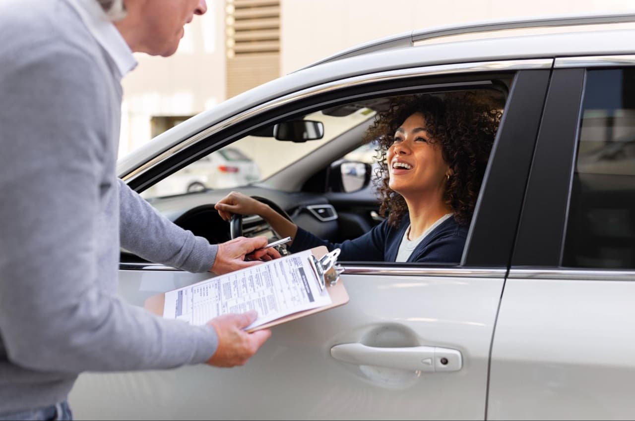 Mulher no carro recebendo orientação de um vendedor, durante uma negociação ou entrega de veículo.