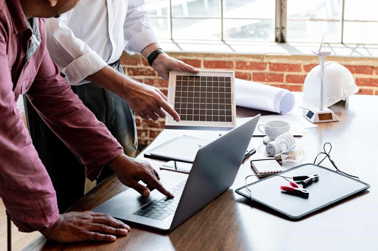 Duas pessoas discutindo um projeto de financiamento para energia solar em uma mesa de trabalho com alguns materiais.
