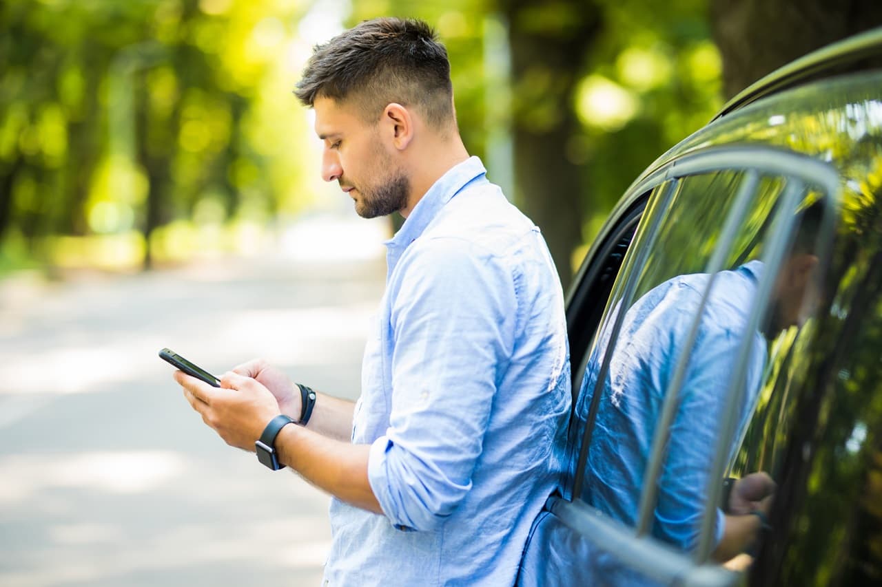 Pessoa consultando informações no celular enquanto está ao lado de um carro estacionado.