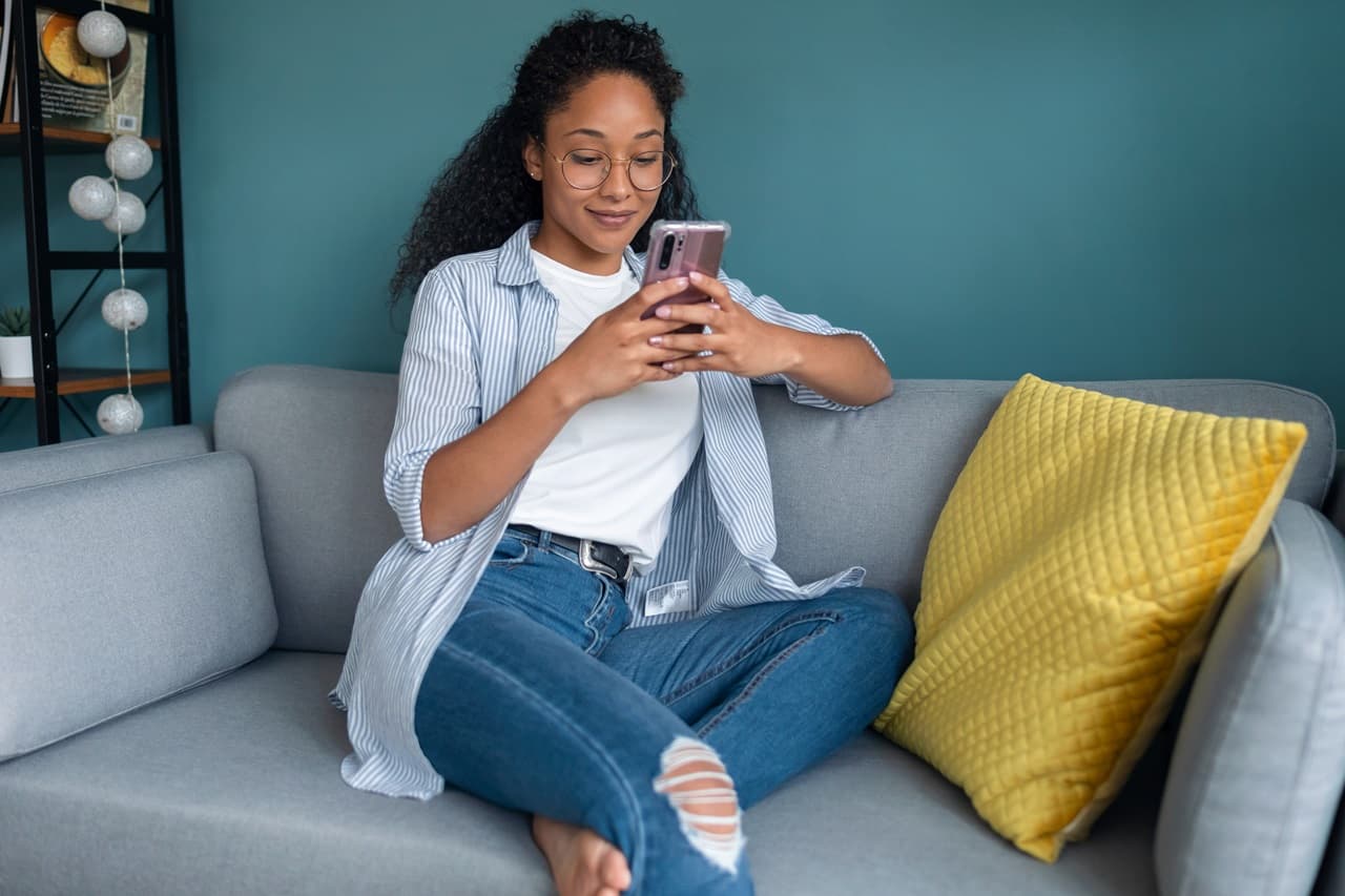 Pessoa sentada em um sofá utilizando um smartphone, em ambiente doméstico, sugerindo organização ou consulta de informações financeiras.