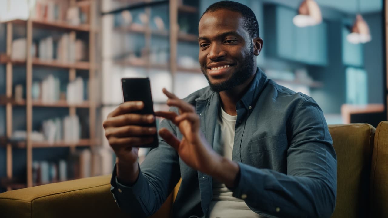 Homem sorrindo sentado em sofá, segurando celular e vendo informações
