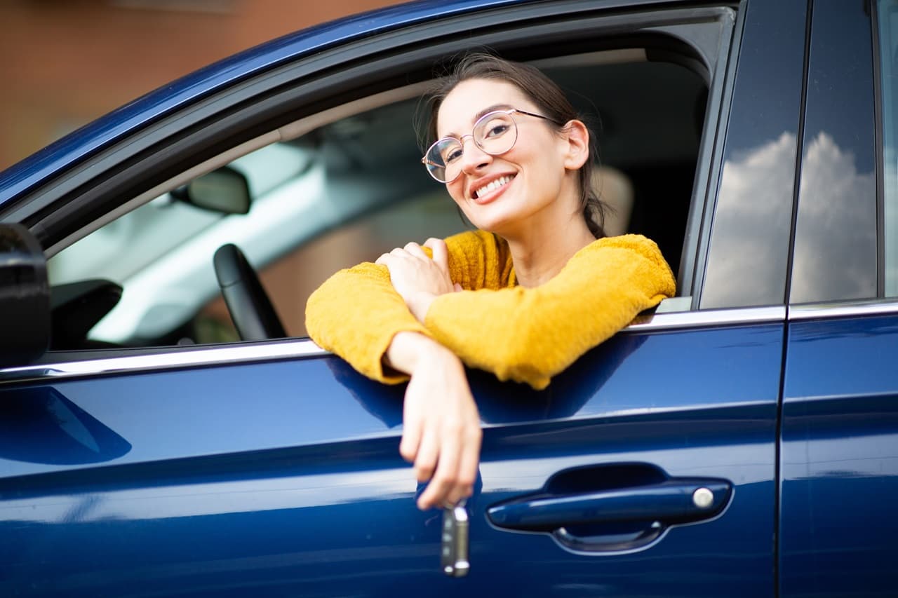 Pessoa apoiada na janela de um carro azul segurando a chave do veículo.