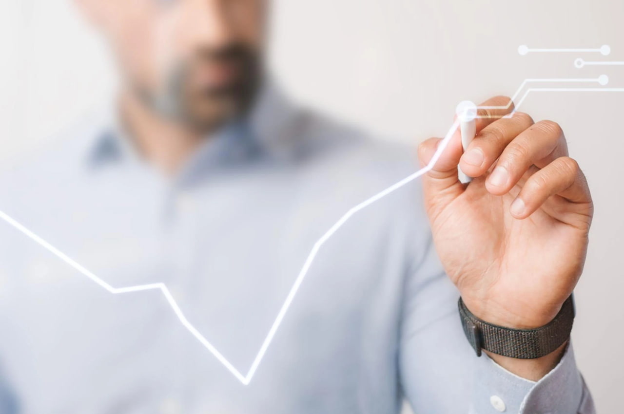 A imagem mostra um homem desfocado em traje social utilizando uma caneta digital para traçar um gráfico de crescimento.