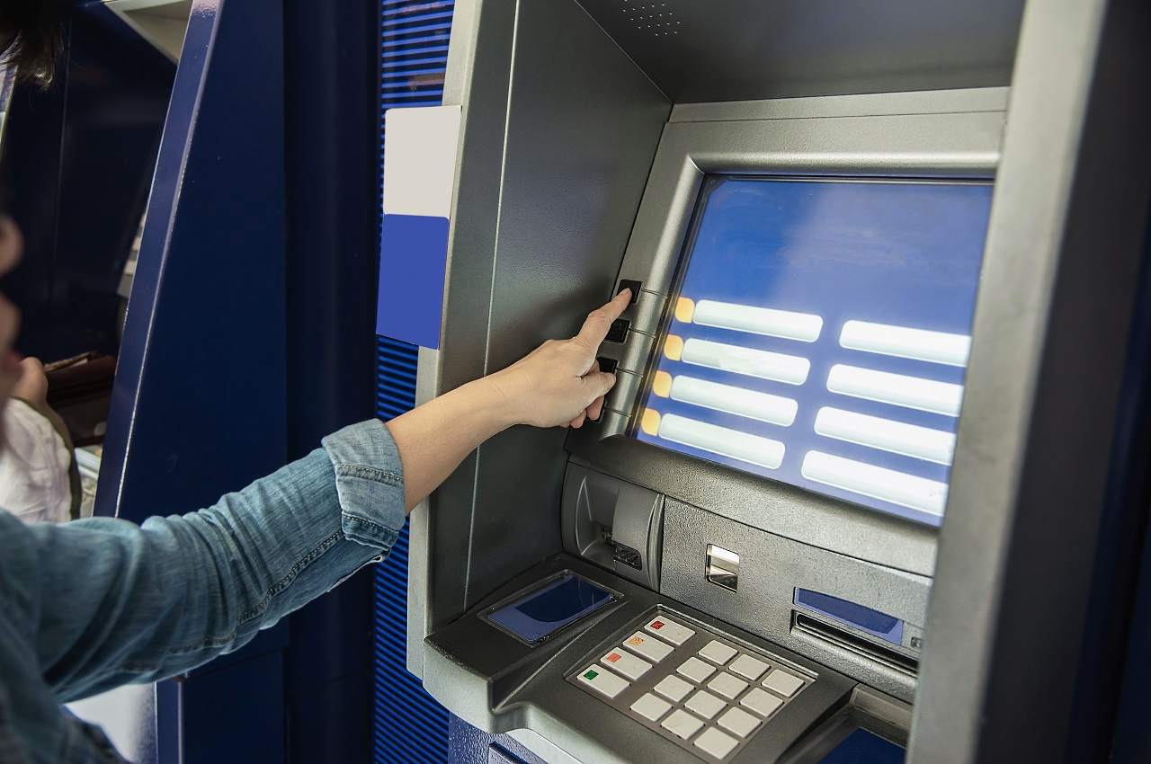 Mulher (rosto não aparece na imagem) tocando em tela touch de caixa eletrônico para sacar saque-aniversário FGTS.