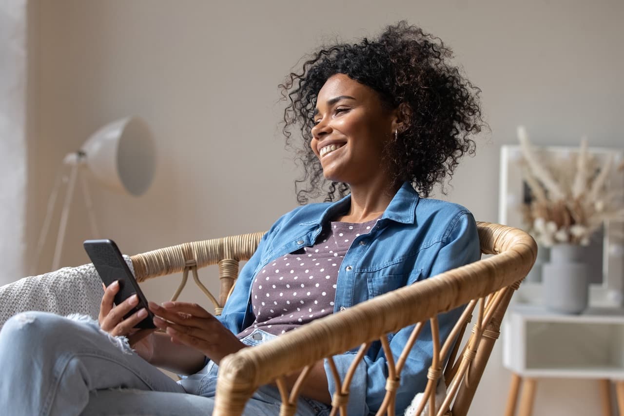 Mulh sentada em cadeira sorrindo, segurando um celular na mão