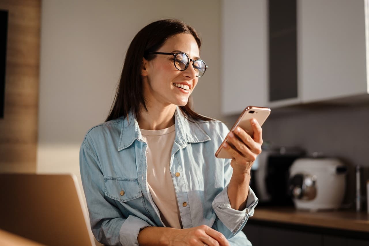 Mulher sentada sorrindo e segurando celular na mão