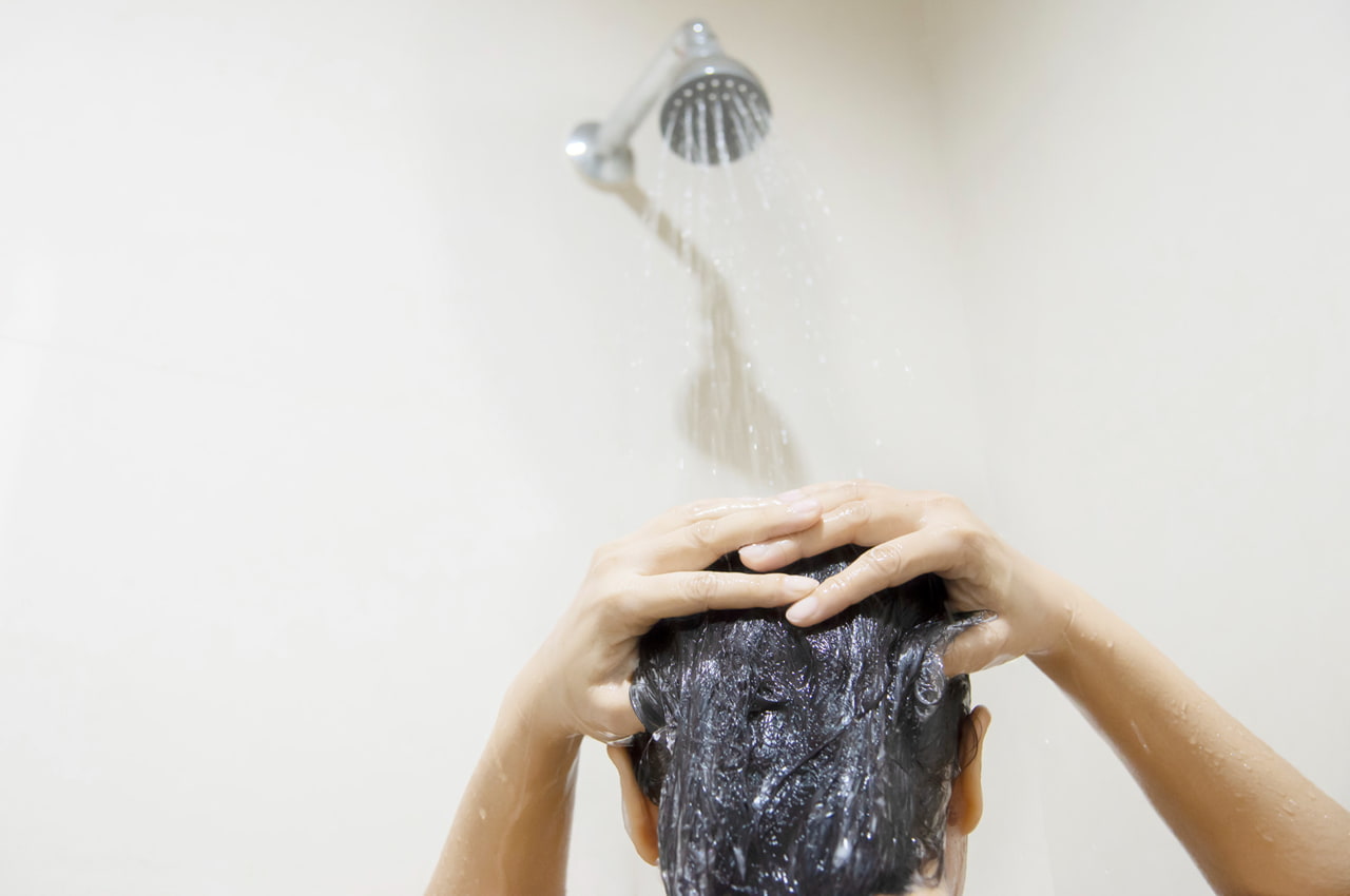 Mulher lavando o cabelo com shampoo no chuveiro.