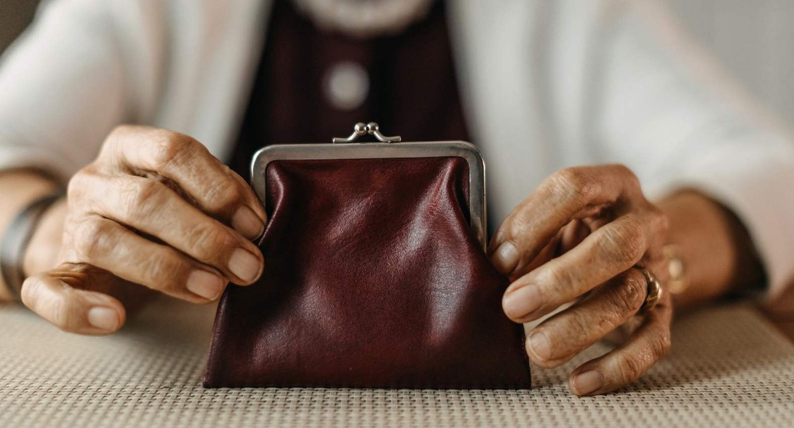 A imagem mostra uma pessoa idosa segurando uma bolsa de guardar moedas.