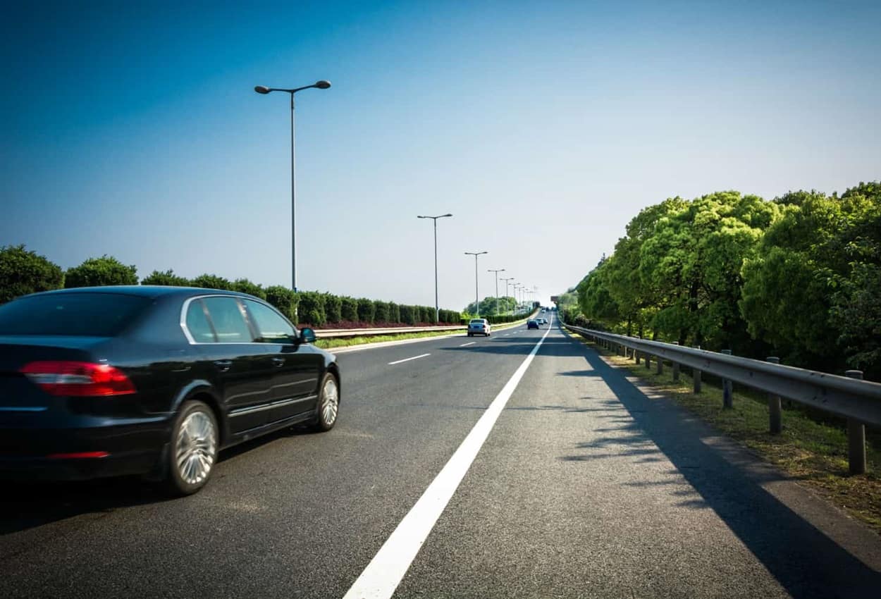 Carro preto trafegando por uma estrada asfaltada durante um dia de céu claro.