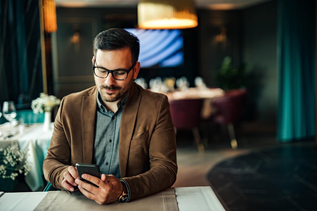 homem sentado com mesa a frente, mexendo no celular