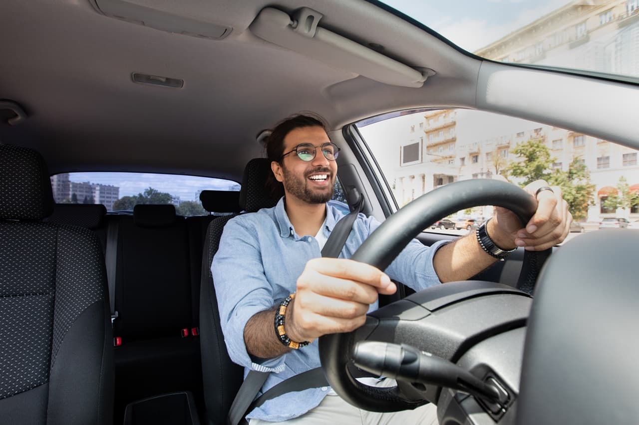 Pessoa dirigindo um carro com as mãos no volante e cinto de segurança.