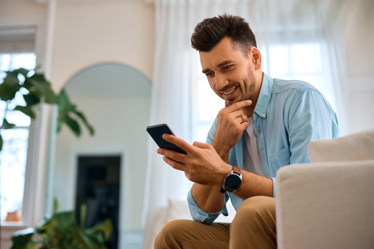 Pessoa sentada em um sofá usando um smartphone em ambiente residencial.