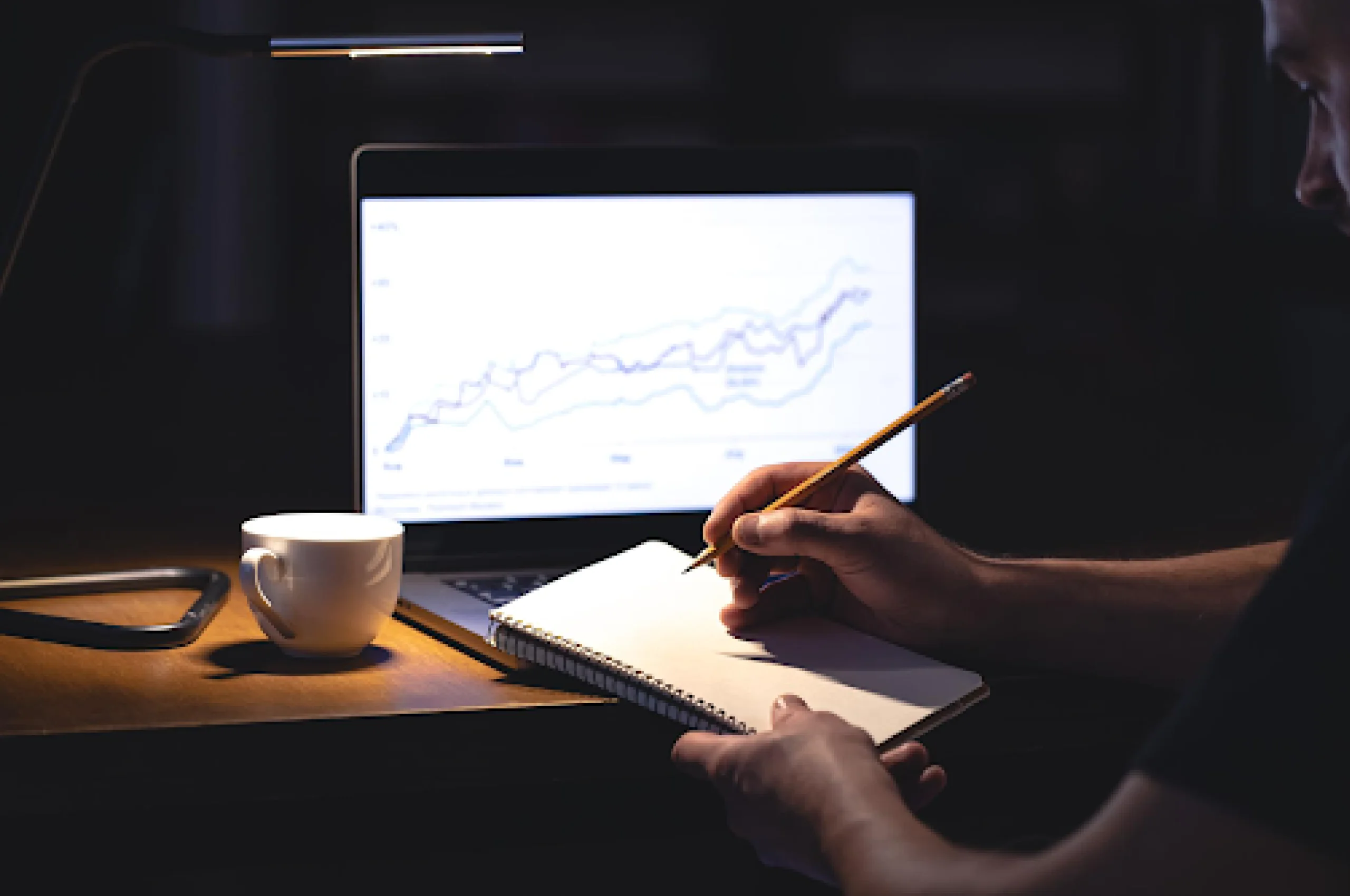 Um homem em frente a um laptop com um gráfico e um bloco de notas à noite, estudando tipos de investidores. 