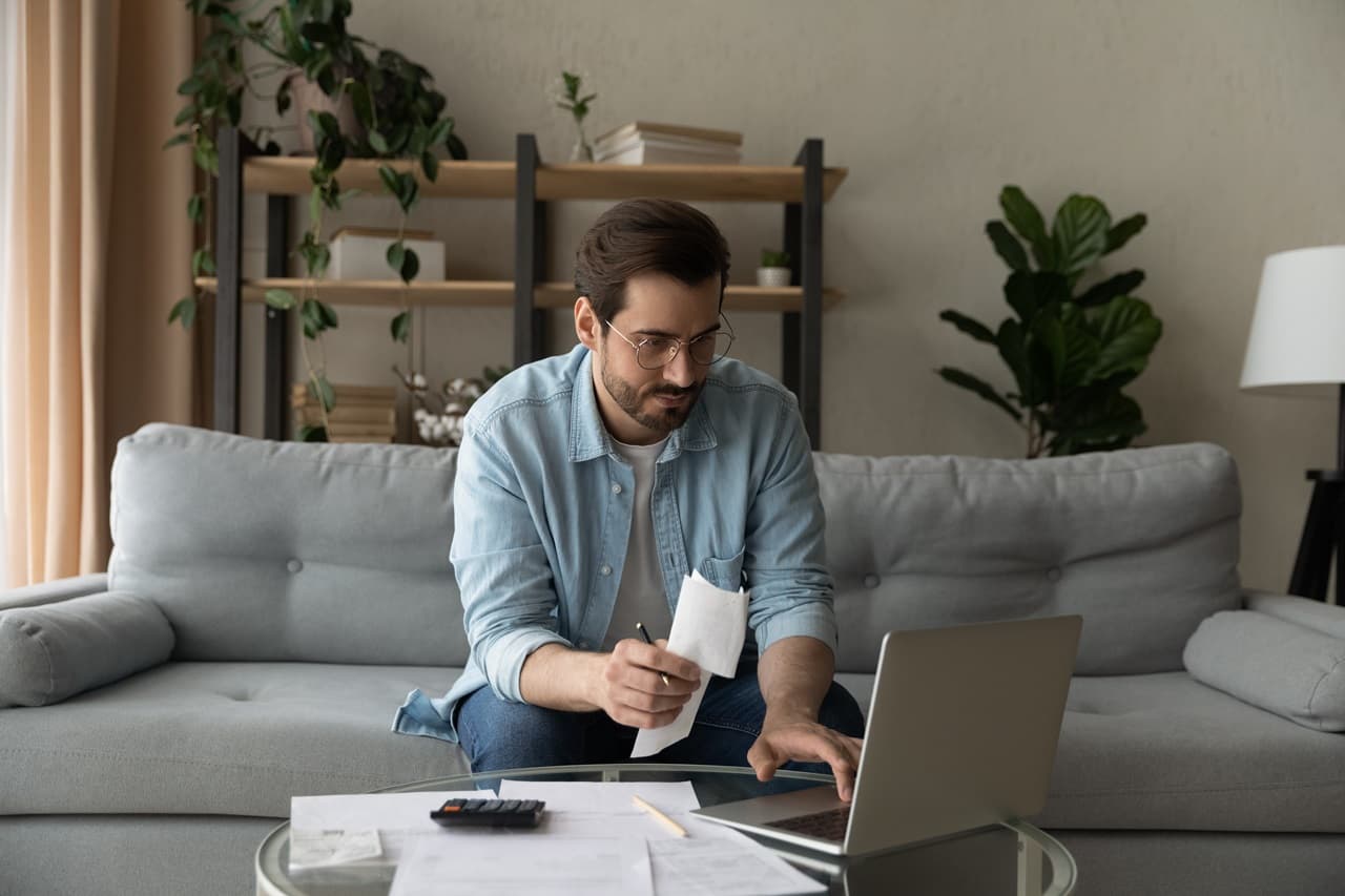 Homem sentado em sofá, analisando informações em um notebook.
