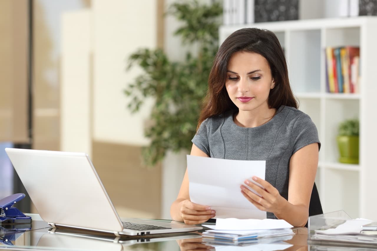 mulher conferindo documento com notebook ao lado