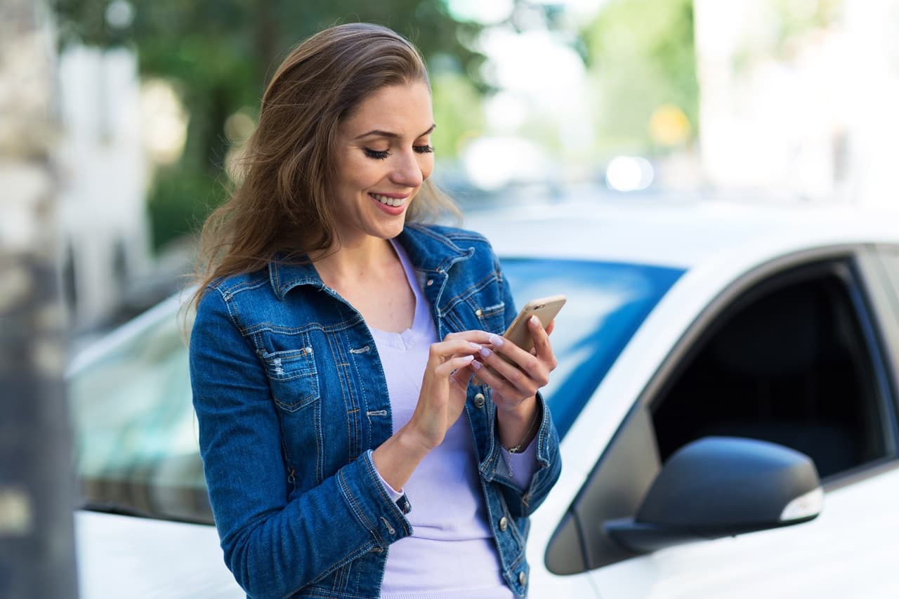mulher em frente ao carro, olhando para celular