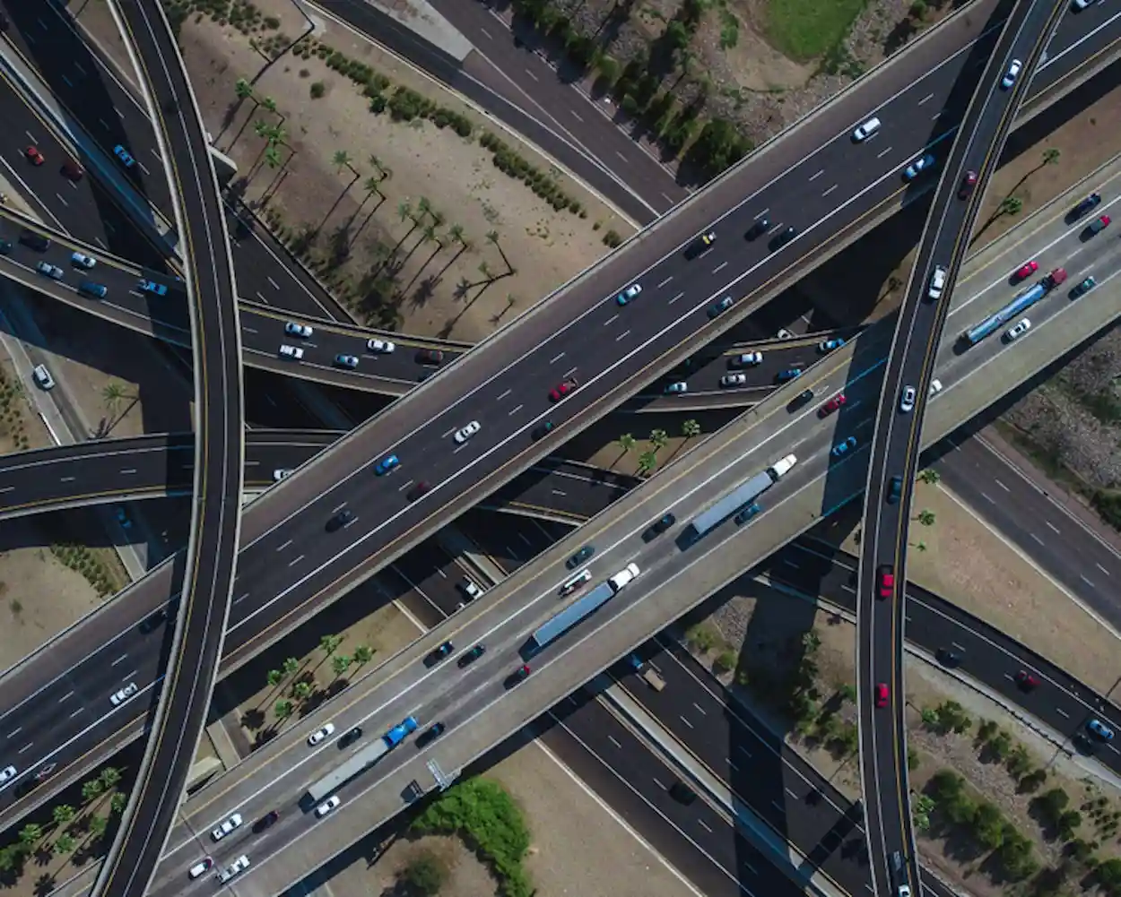 Vista aérea de uma rede de viadutos e pontes com várias pistas, viaturas coloridas e sombras projetadas pelas estruturas, formando interseções.
