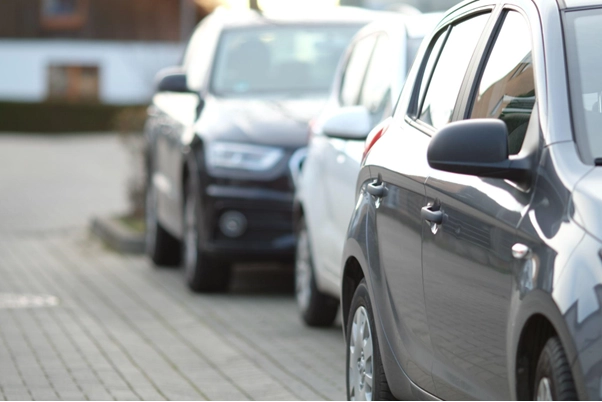 Filas de carros estacionados em linha numa rua, com foco suave no veículo da frente e imagem desfocada ao fundo, sugerindo trânsito ou estacionamento.