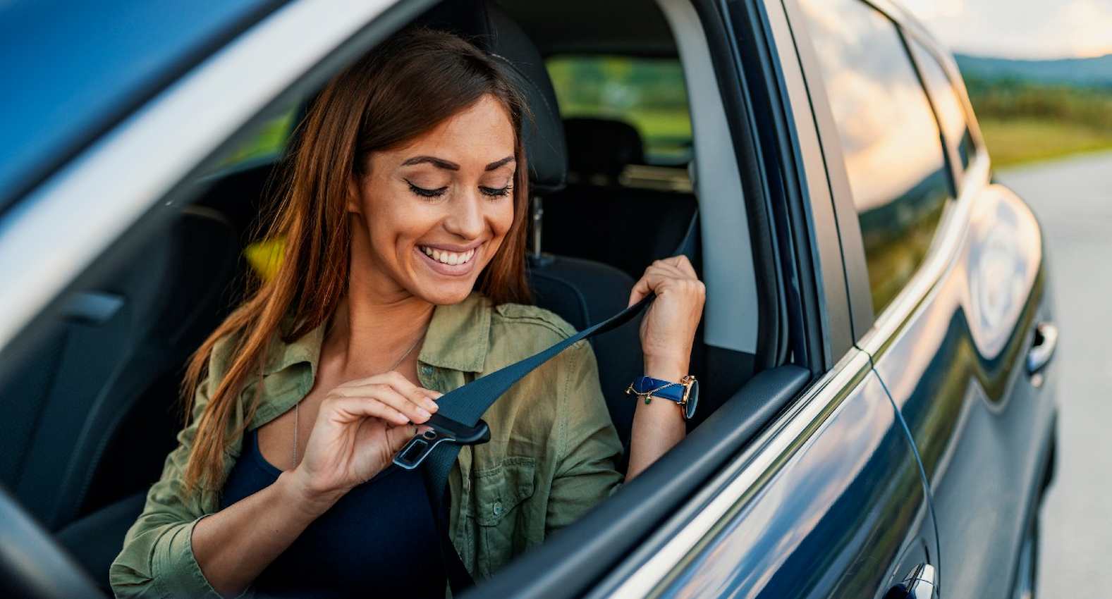 A imagem mostra uma mulher dentro de seu carro, colocando o cinto de segurança.