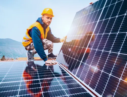 Um homem com camisa azul, colete e capacete de segurança amarelos, fazendo a instalação de placas solares.